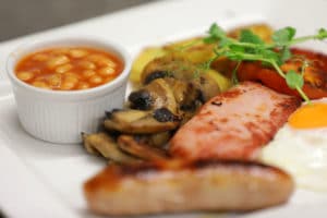 A plate showing gluten-free sausage, mushrooms, bacon, beans and microgreens
